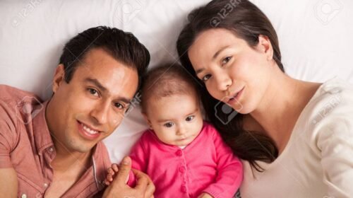 Portrait from above of a beautiful young Latin family with a baby girl relaxing in a bed at home