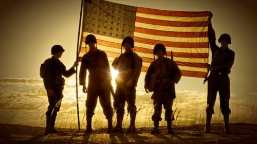 Four WWII Soldiers Holding up a translucent American Flag at sundown.  The sun  behind the flag creates a semi-silhouette of the four war weary soldiers.  Clouds, sun, and sand complete the picture.  All soldiers are in uniform with helmets and rifles, boots etc.
