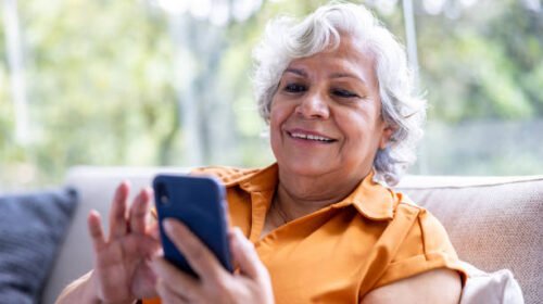 Happy Latin American senior woman texting on her cell phone and smiling at home - lifestyle concepts