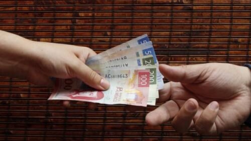 one hand paying with mexican banknotes and another hand receiving the money
